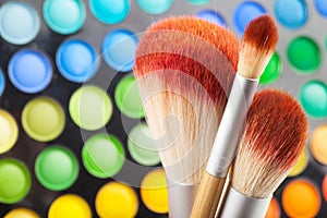 Makeup brushes and set of colorful eye shadows as background