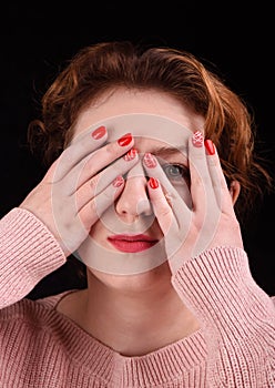 Makeup concept. Close-up photo of a beautiful girl closes her eyes with her palms and spies