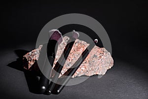 Makeup cosmetic brushes lie on granite stone on black background. Set of different cosmetic brushes