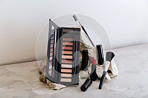 Makeup cosmetics on stone pedestal. Red scarlet lipstick eyeshadow makeup brushes on gray concrete background. Minimal