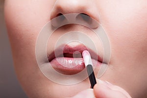 Makeup. Girl applying lipgloss lipstick on lips. Part of face.