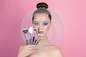 Makeup of a girl& x27;s face close-up in the studio on a pink background in the hands of a brush and paint. A young girl