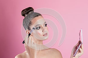 Makeup of a girl& x27;s face close-up in the studio on a pink background in the hands of a brush and paint. A young girl