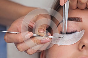 Makeup Master corrects, and strengthens eyelashes beams, holding out a pair of tweezers in a beauty salon.