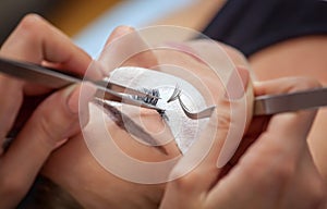 Makeup Master corrects, and strengthens eyelashes beams, holding out a pair of tweezers in a beauty salon.