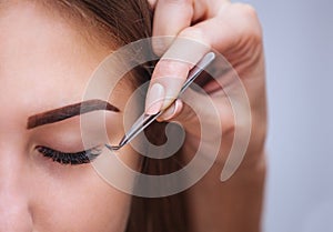 Makeup Master corrects, and strengthens eyelashes beams, holding out a pair of tweezers in a beauty salon photo