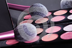 Makeup palette and brush reflect in mirror.