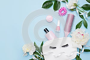 Makeup products with cosmetic bag and flowers on color blue background, copy space