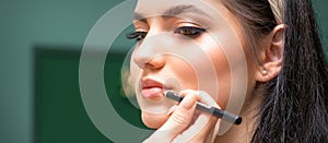 Makeup professional artist or cosmetologist is painting contour lips of a young woman with a pencil close up.