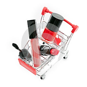 Makeup in pushcart on white background. Red lipstick, mascara, pink lip gloss, powder, nail polish. Makeup products in sh