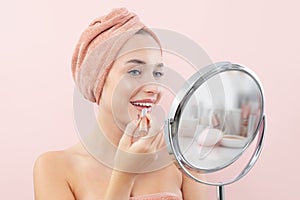 Makeup, smiling young pretty woman applying the red lipstick on the lips, wears a towel wrapped on head and with her big blue eyes