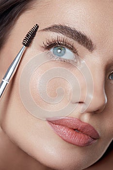 Makeup. Woman Brushing Eyebrows With Brush Close Up Portrait. Beautiful Brunette With Perfect Skin.