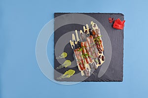 Maki sushi rolls set over black tray. California or philadelphia sushi set served with pickled ginger and wasabi sauce