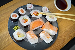 Maki on a wooden table on black slate plate with soy sauce and c