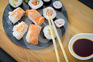 Maki on a wooden table on black slate plate with soy sauce and c