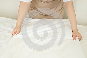 Making bed, chambermaid in bedroom straightens bed linen, hotel room service
