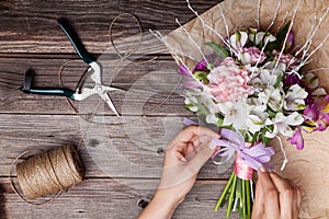 Making a bouquet from gillyflowers and alstroemeria on old wooden background with wooden heart and scissors with paper
