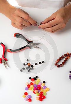 Making a bracelet of colorful beads. Female hands with a tool on a white background.