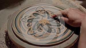 Making a clay plate. Painting at rotating circle. Potter drawing beautiful art using one finger. Handmade ukrainian