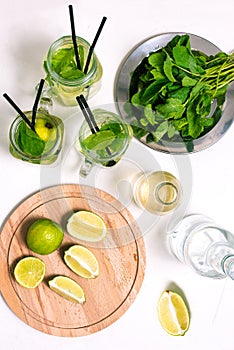 Making a cold summer mojito drink with lime, mint leaves, straw, ice cubes, soda and rum on a white background