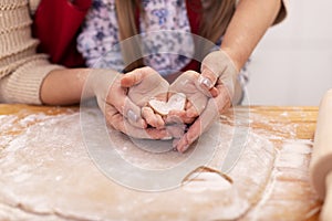 Making cookies with love - woman and little girl hands hold heart shaped gingerbread cookie