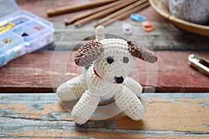 Making crochet white dog. Toy for babies or trinket.  On the table threads, needles, hook, cotton yarn. Handmade gift. DIY crafts