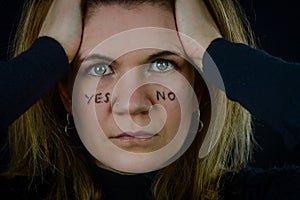 making decisions - portrait of a beautiful blonde woman with yes and no written on her cheeks and intently looking for answer