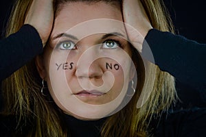 making decisions - portrait of a beautiful blonde woman with yes and no written on her cheeks and intently looking for answer