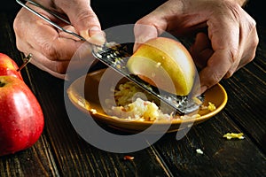 Making a dessert from applesauce. Close-up of a chef hands grating a fresh apple with a grater