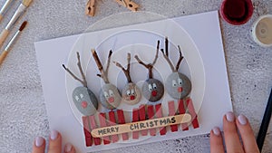 Making Diy Merry Christmas deer on greeting card postcard made of pebbles, sea stones, clothespins and branches on white