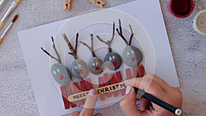 Making Diy Merry Christmas deer on greeting card postcard made of pebbles, sea stones, clothespins and branches on white