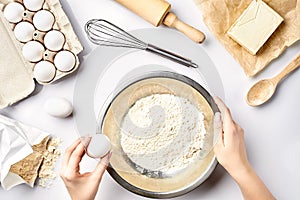 Making dough top view. Overhead of baker hands break egg on flour. Cooking ingredients for pastry on white table.