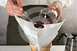 Making drip coffee. Woman adding ground coffee into chemex coffeemaker with paper filter, closeup