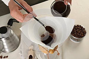 Making drip coffee. Woman adding ground coffee into chemex coffeemaker with paper filter at white table, closeup