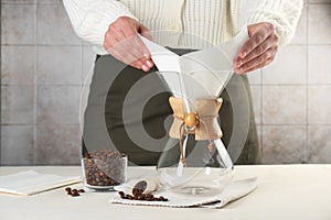 Making drip coffee. Woman setting paper filter into glass chemex coffeemaker at table, closeup