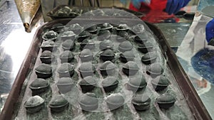 Making dumpling in modern foodstuff manufacturing. Chef hands putting ready dumplings of black color on tray. Homemade