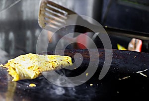 Making of egg roll on a hot frying pan with oil and paratha and salad