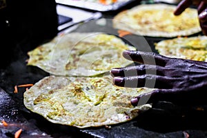 Making of egg roll on a hot frying pan with oil and paratha and salad