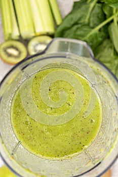 Making a green smoothie with celery, kiwi, apple and spinach in a blender, top view.