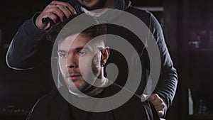 Making haircut look perfect. Young bearded man getting haircut by hairdresser while sitting in chair at barbershop