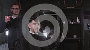 Making haircut look perfect. Young bearded man getting haircut by hairdresser while sitting in chair at barbershop