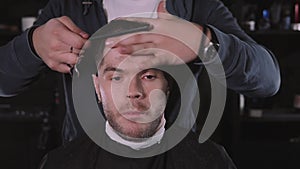 Making haircut look perfect. Young bearded man getting haircut by hairdresser while sitting in chair at barbershop