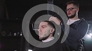 Making haircut look perfect. Young bearded man getting haircut by hairdresser while sitting in chair at barbershop