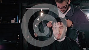 Making haircut look perfect. Young bearded man getting haircut by hairdresser while sitting in chair at barbershop