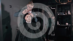 Making haircut look perfect. Young bearded man getting haircut by hairdresser while sitting in chair at barbershop