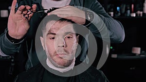 Making haircut look perfect. Young bearded man getting haircut by hairdresser while sitting in chair at barbershop