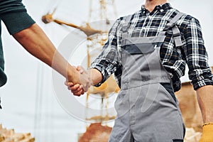 Making handshake. Two construction workers in uniform and safety equipment have job on building together