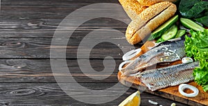 Making herring fillet sandwich with onions, cucumber and salad on a wooden board. Dark wooden background with copy space for text