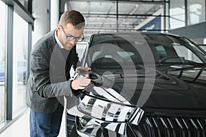 Making his choice. Horizontal portrait of a young man in a suit looking at the car and thinking if he should buy it