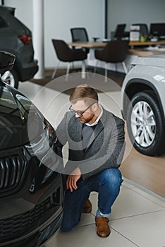 Making his choice. Horizontal portrait of a young man in a suit looking at the car and thinking if he should buy it